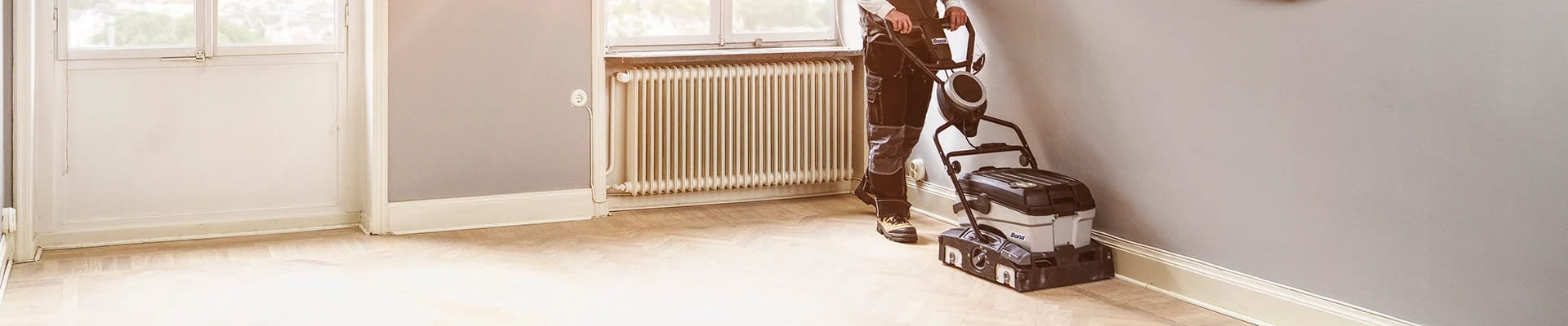 A flooring professional uses a Bona Power-Scrubber to professionally clean a white, herringbone parquet hardwood floor.