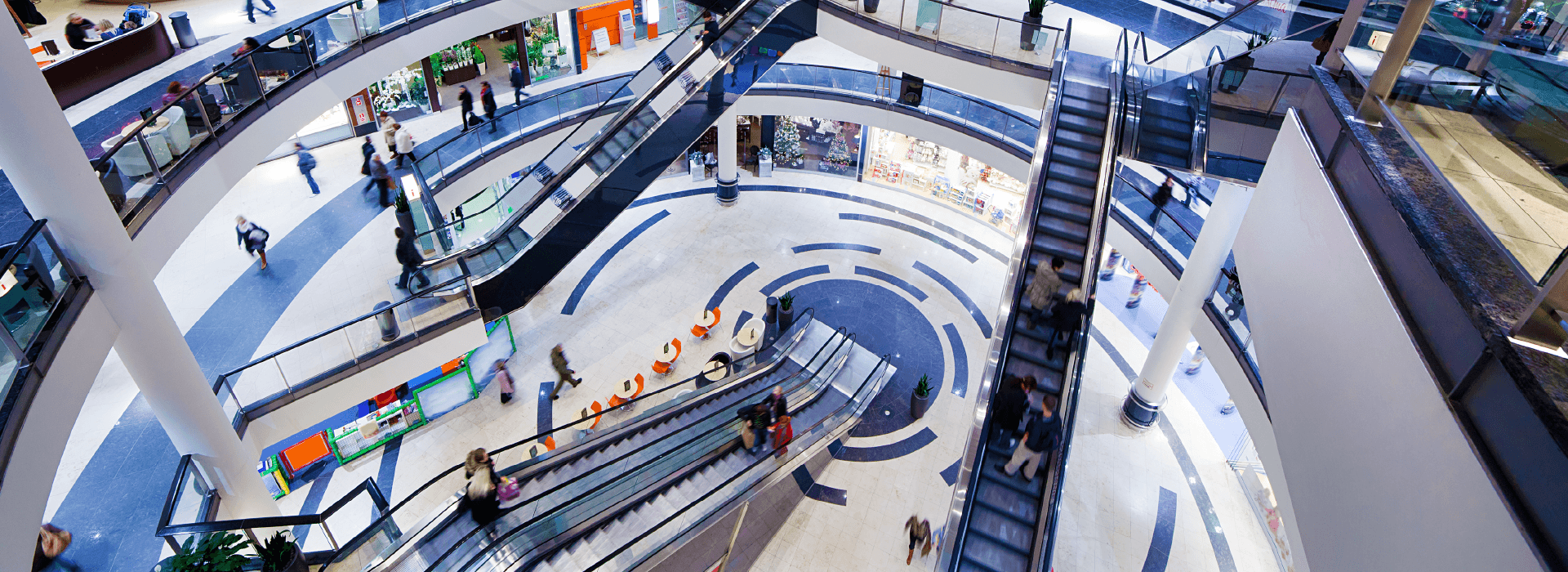 Third-level view of a colorful mall atrium, showcasing shops, escalators, and a stunning resilient ground floor.