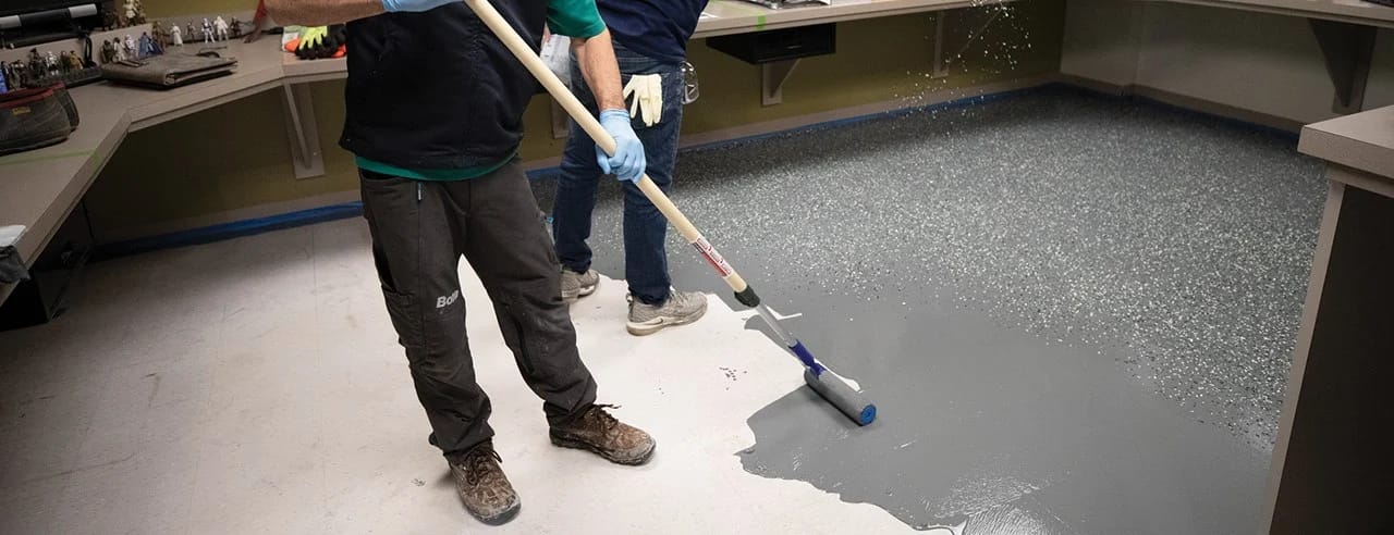 Contractors carefully apply a Bona resilient floor coating to restore an aged linoleum floor in a commercial space.