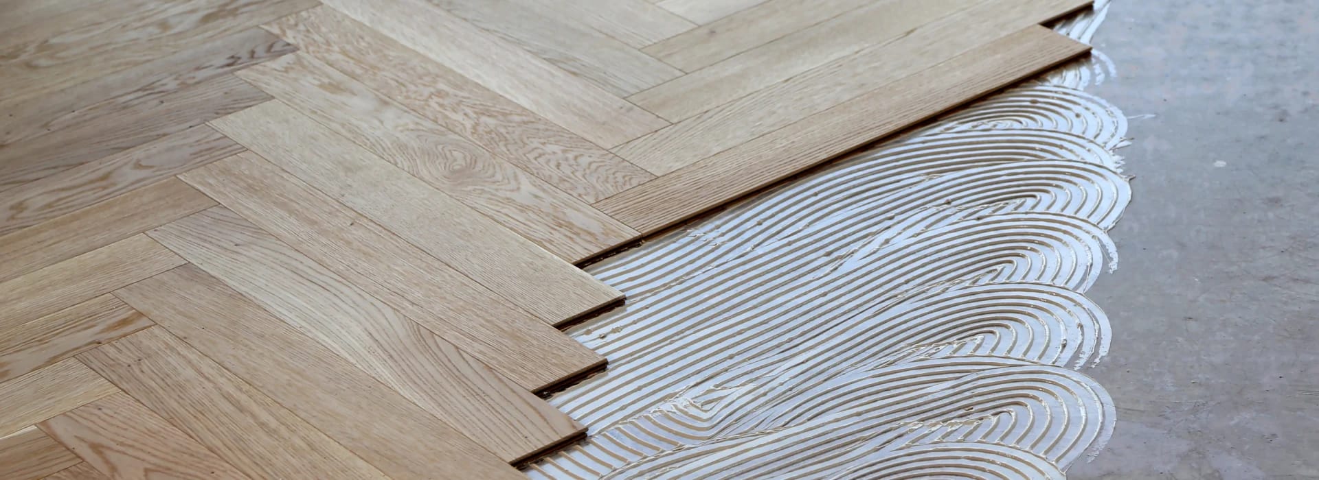 A subfloor section has been prepped with a Bona silane-based adhesive next to new floorboards that have been installed.