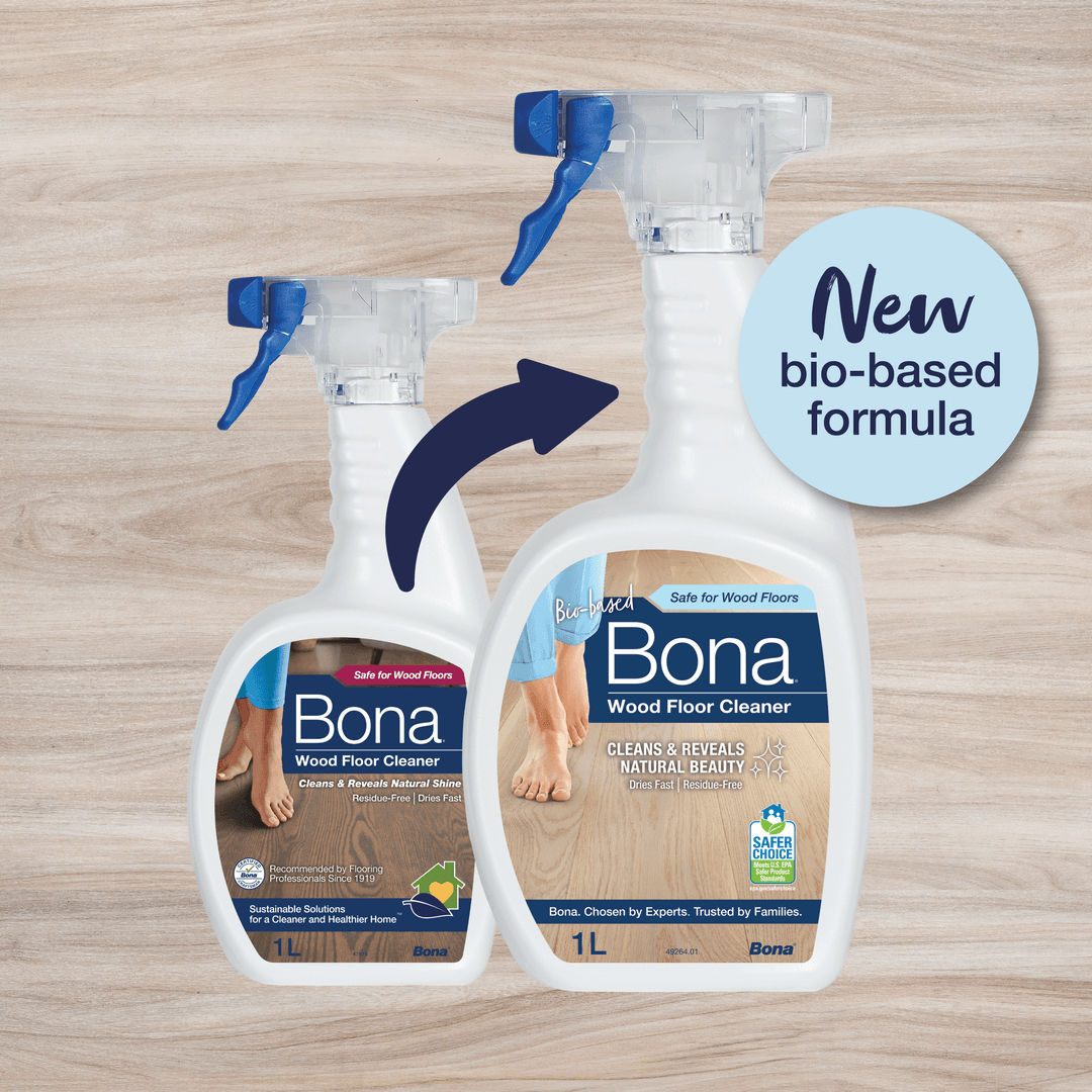 Two spray bottles of Bona Wood Floor Cleaner are shown side by side on a light wood surface. An arrow points from the smaller, older version on the left to a larger, updated version on the right. A circular label reads "New bio-based formula", highlighting the updated product.
