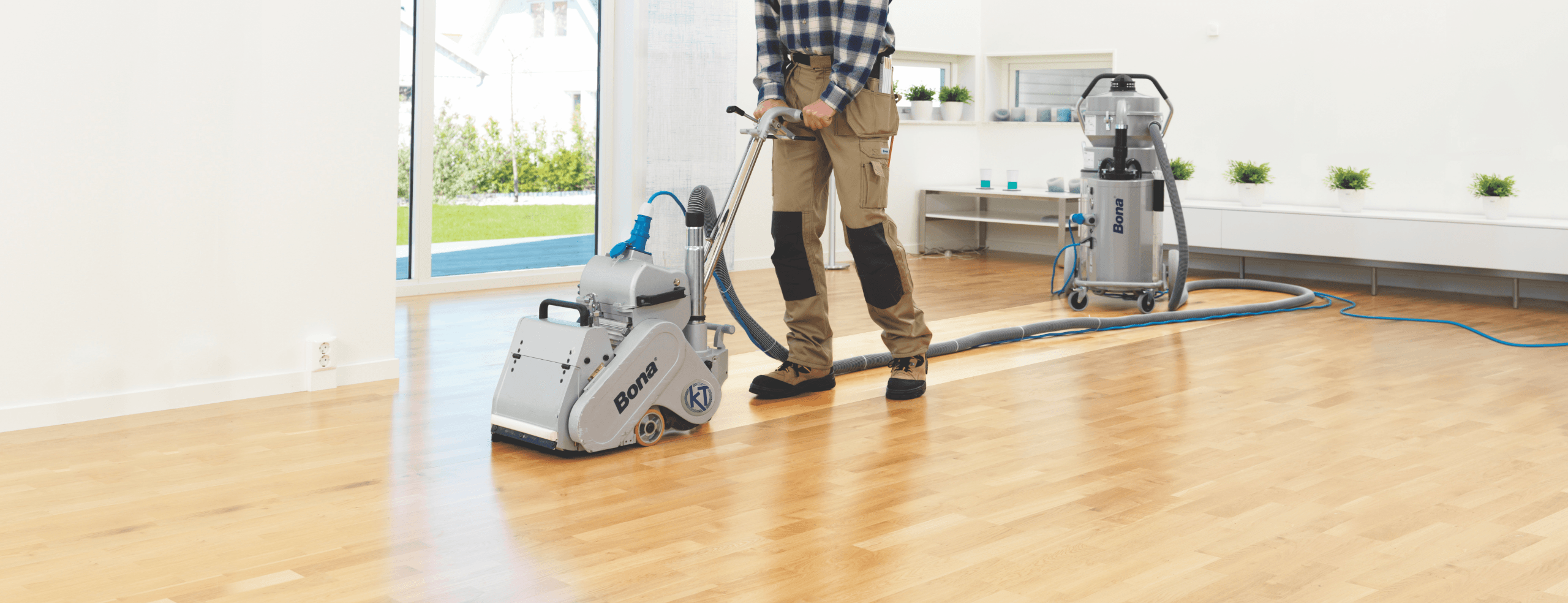 A flooring craftsman uses a Bona Belt sanding machine with a Bona Portable DCS to remove the finish from a hardwood floor.